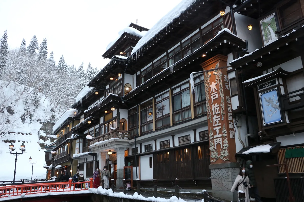 2022年1月、銀山温泉の銀山川沿いに並ぶ雪に覆われた木造旅館。能登屋旅館の塔と赤い橋。