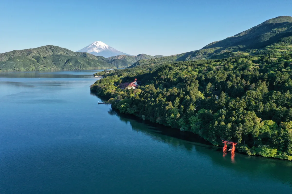 Lake Ashi in Hakone seen from above, with the red Hakone Shrine torii at the water's edge and snow-capped Mount Fuji in the.