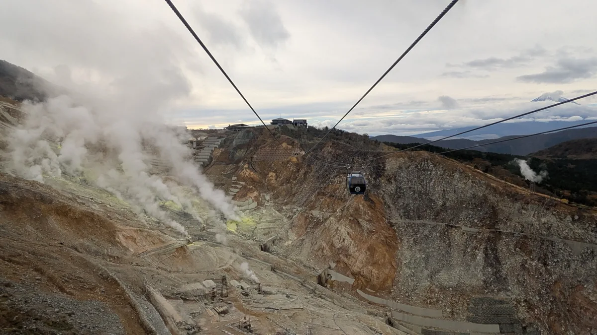 The steaming volcanic valley of Owakudani in Hakone, with a Hakone Ropeway gondola passing overhead on its cables, in 2025