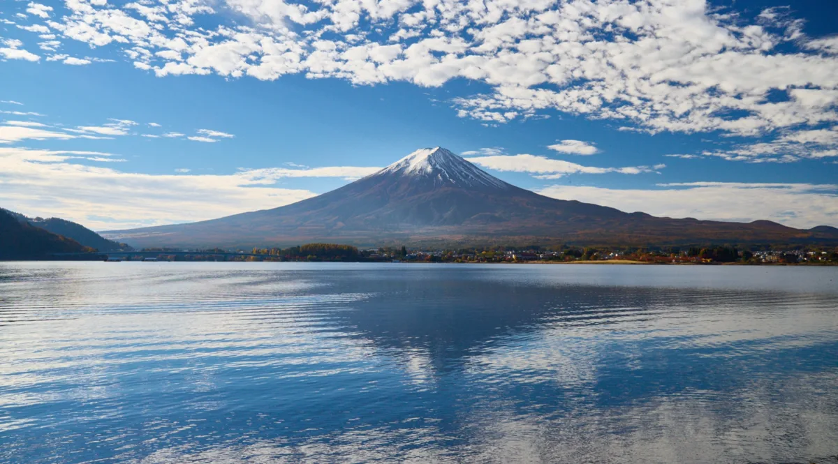 Mount Fuji seen across a calm Lake Kawaguchi under a cloudy blue sky, in 2025