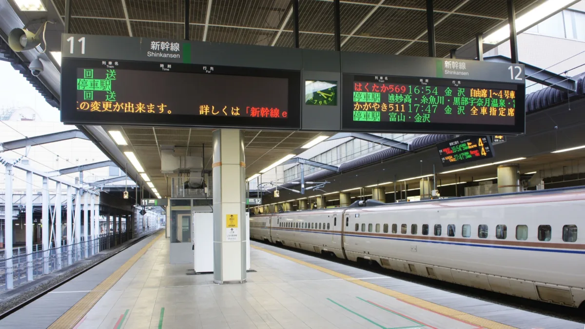 A departure board at Nagano Station showing a Hakutaka to Kanazawa with non-reserved cars 1 to 4 and a Kagayaki to Kanazawa.