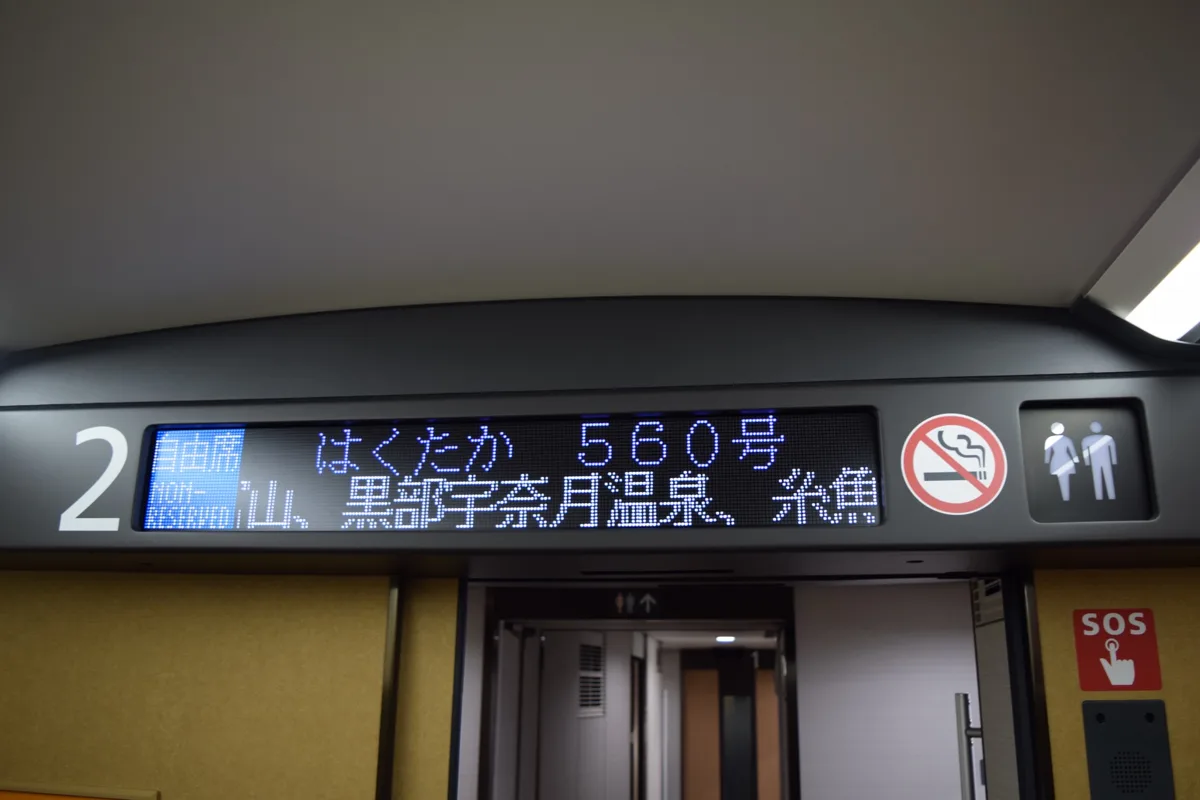The display inside car 2 of a W7 series train showing Hakutaka 560 and Non-Reserved, with stops at Toyama.