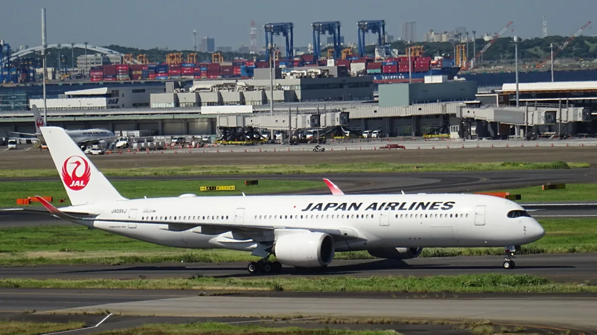 A Japan Airlines Airbus A350-900 in the current red crane livery taxiing at Haneda Airport, with container cranes in the.