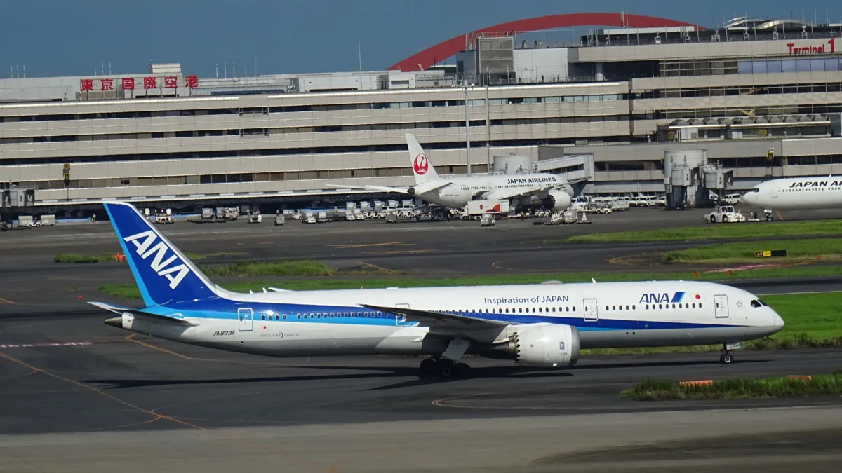 An All Nippon Airways Boeing 787-9 in the standard blue livery taxiing in front of Haneda Airport Terminal 1, with JAL.