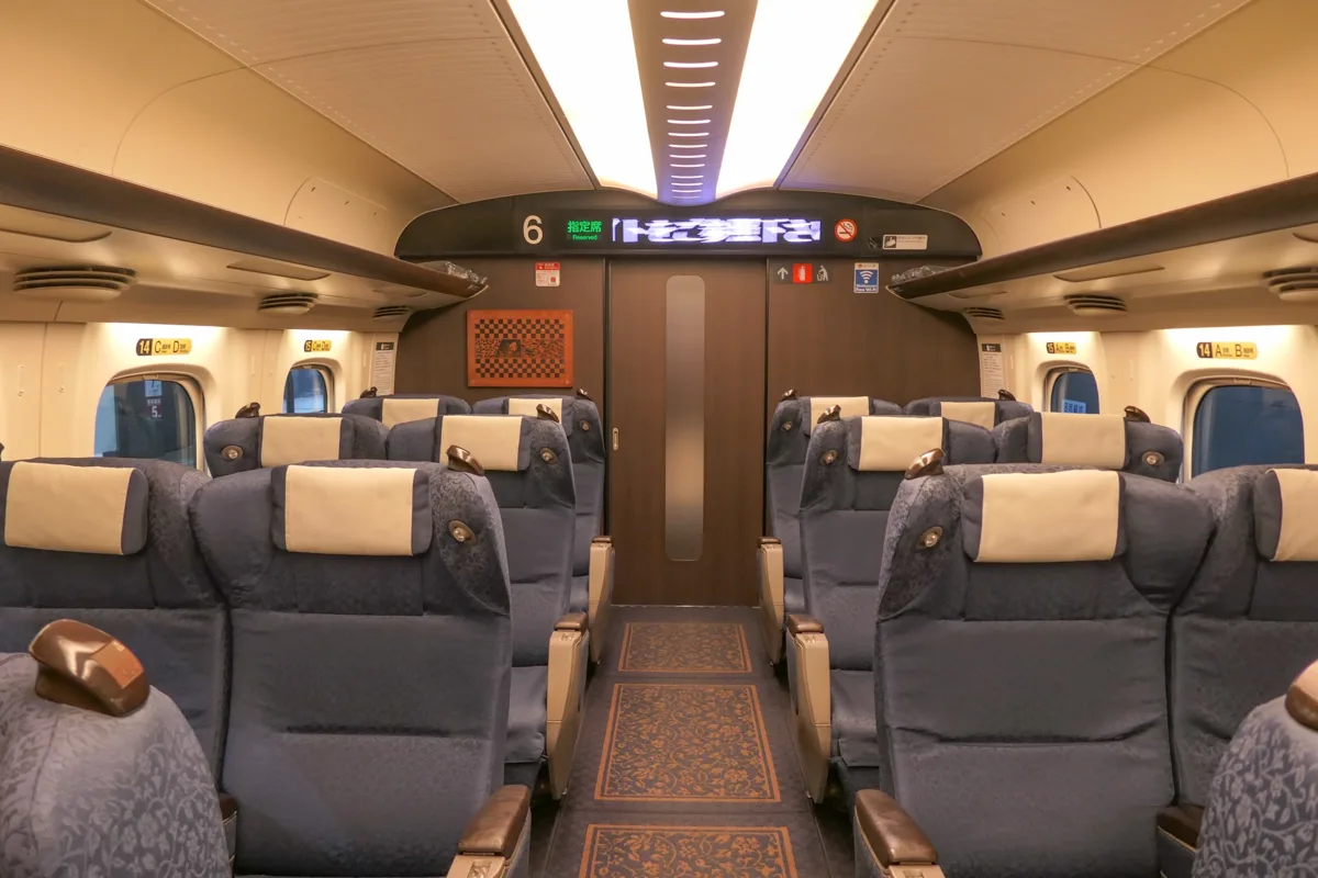 Green Car interior of an N700-7000 series Kyushu and Sanyo Shinkansen, with grey seats in rows of two and a patterned.