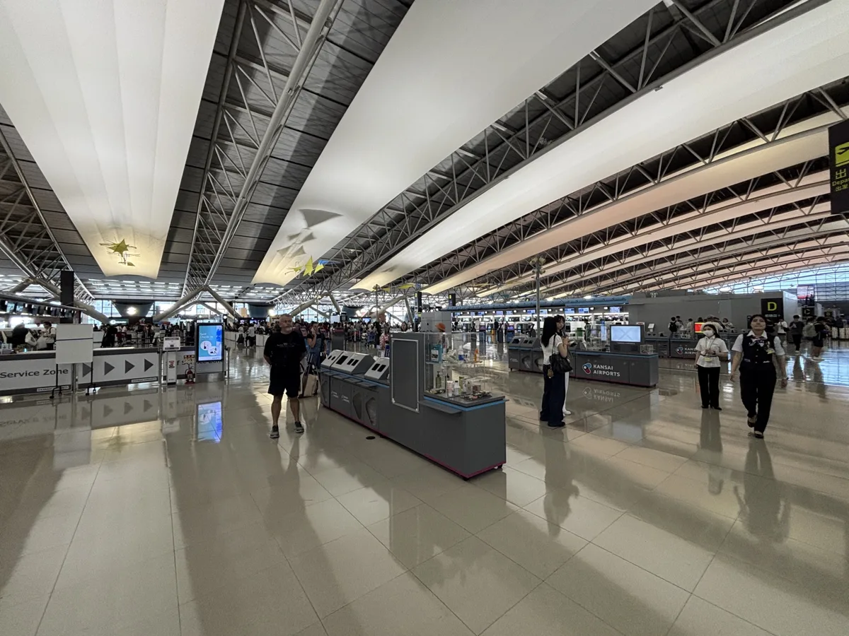 The departure hall of Kansai International Airport Terminal 1 under its long curved roof, in 2025