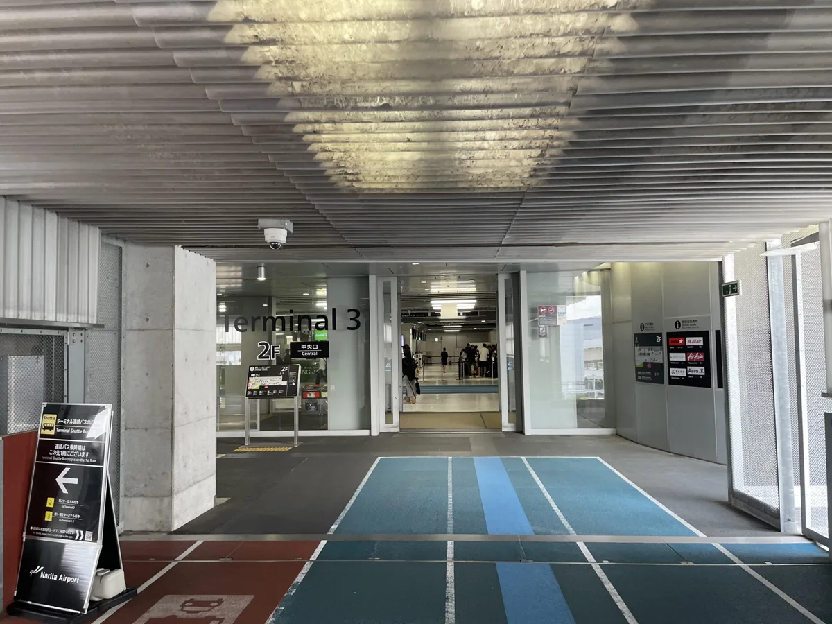 The covered walkway to Narita Airport Terminal 3, with blue running-track style lanes on the floor, in 2024