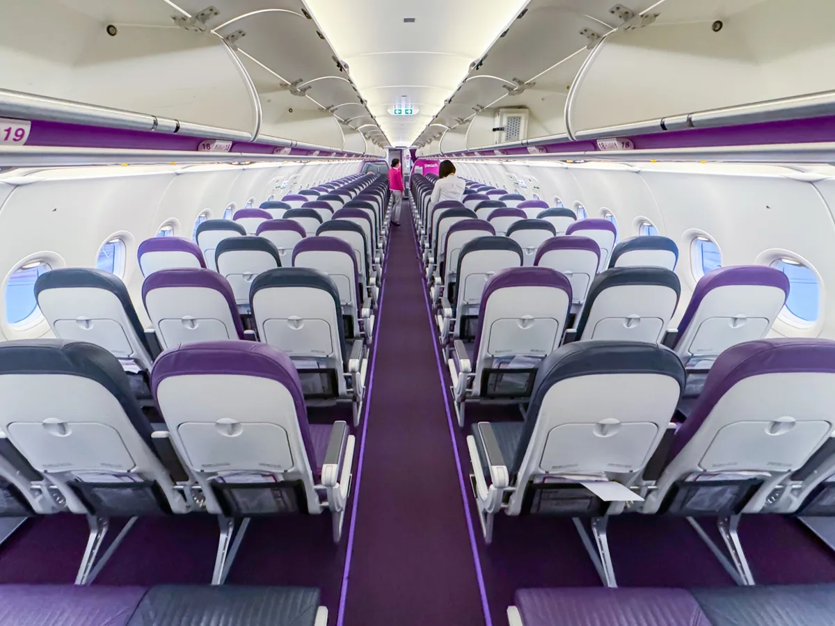 The cabin of a Peach Aviation Airbus A320neo, with grey and purple seats in rows of three on each side of the aisle, in 2023