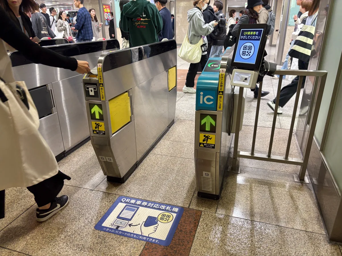 A passenger reaching out to touch the reader of a ticket gate with an IC reader and a QR code reader, at JR Nagoya Station.