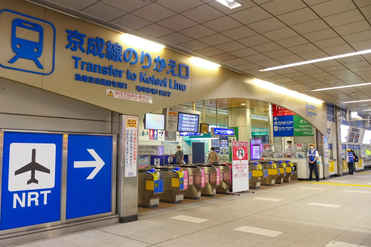 The Keisei Line transfer gates at Nippori Station, with a sign reading Transfer to Keisei Line and an airplane NRT arrow, in.