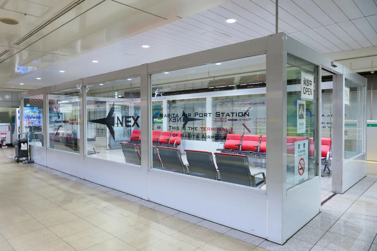 The glass-walled N'EX waiting room on the JR platform at Narita Airport Terminal 1 Station, with red seats, in 2021