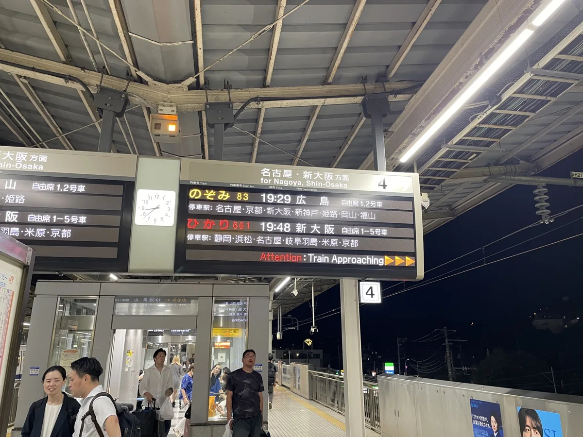 A departure board at Shin-Yokohama Station showing a Nozomi to Hiroshima and a Hikari to Shin-Osaka, with their stops, in.