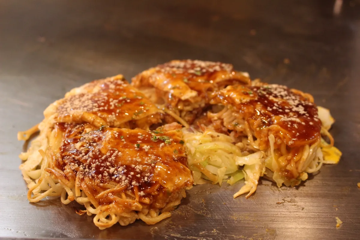 A Hiroshima-style okonomiyaki layered with noodles and cabbage on a hot plate in Hiroshima, in 2016