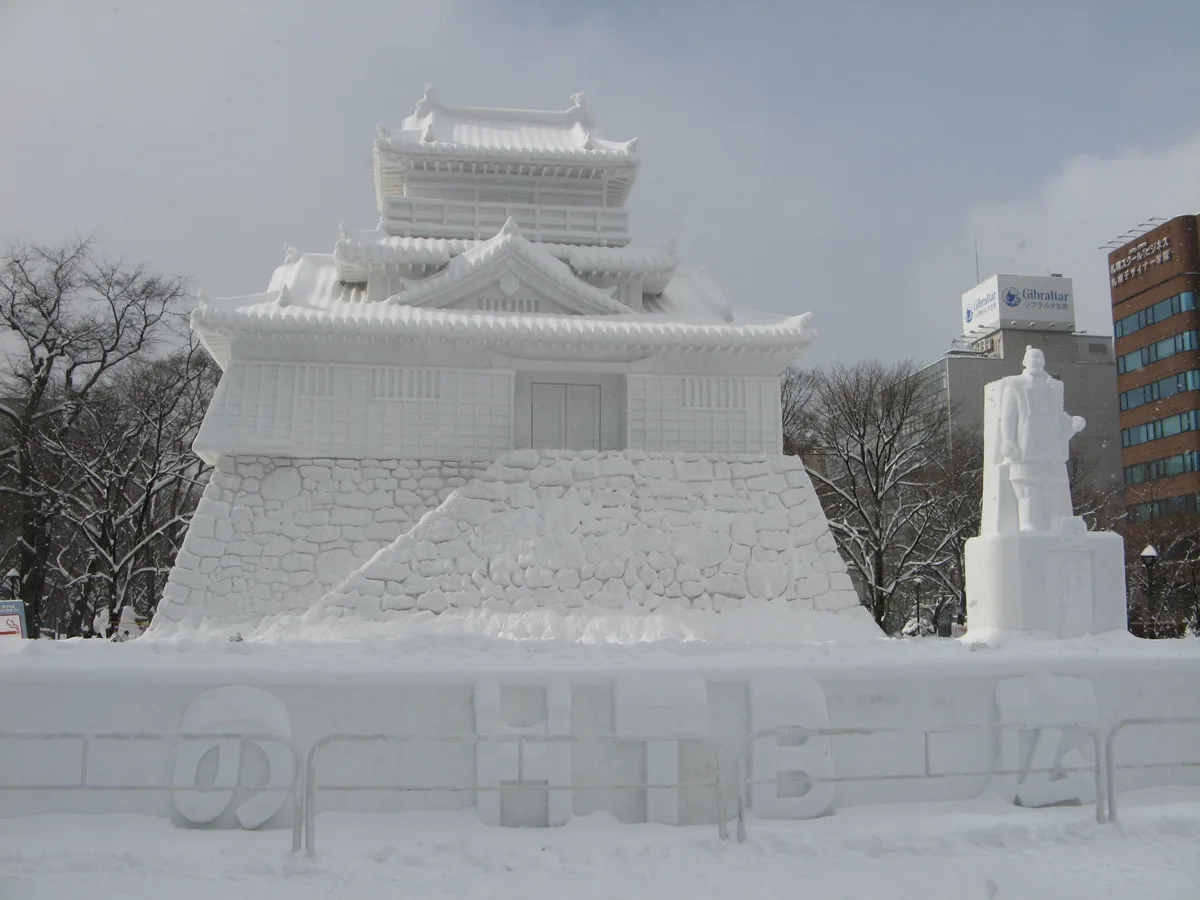 A large snow sculpture of a Japanese castle at the Odori site of the Sapporo Snow Festival, with office buildings behind