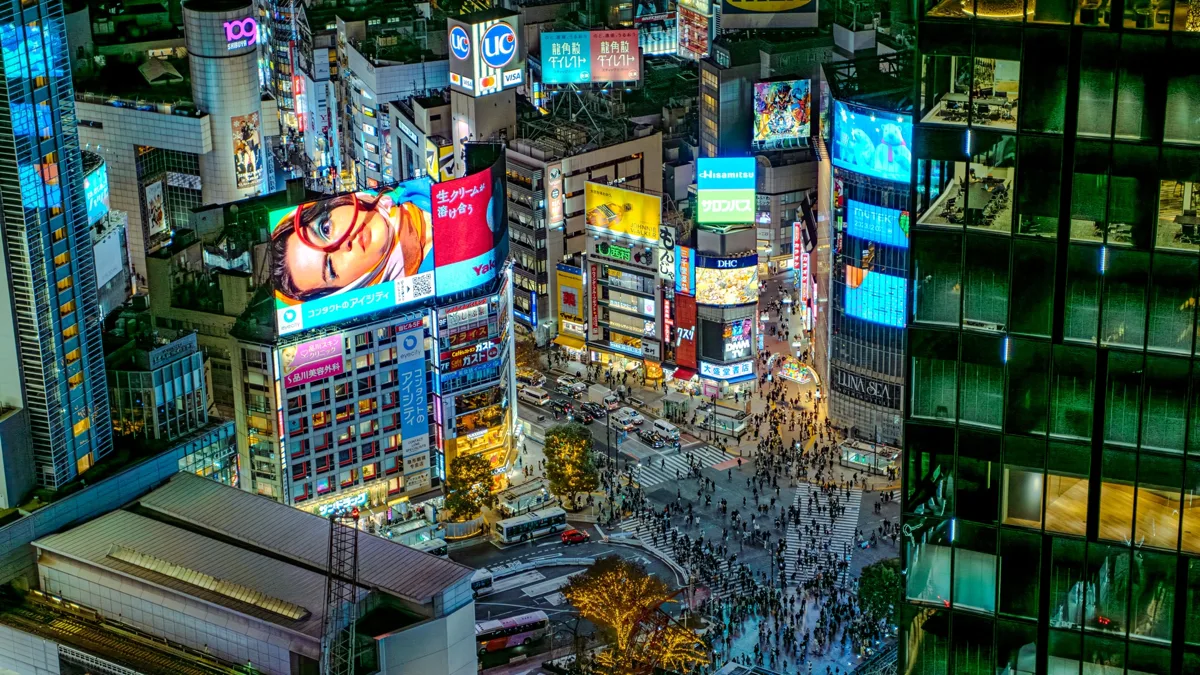 The Shibuya Scramble Crossing seen from above at dusk, with lit-up billboards and people crossing in all directions, in 2023