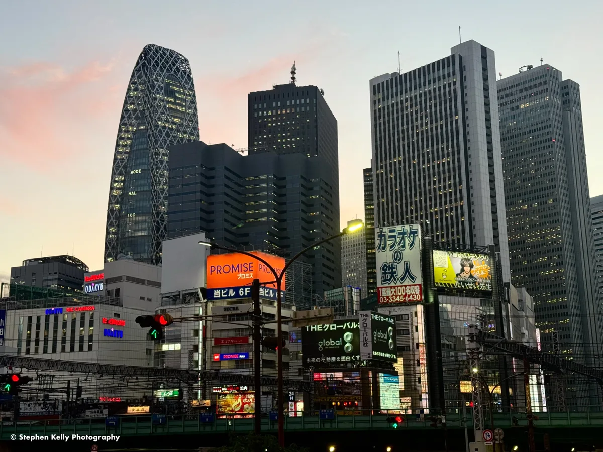 The skyscrapers of Nishi-Shinjuku at dusk, including the Mode Gakuen Cocoon Tower, with lit shop signs below, in 2023