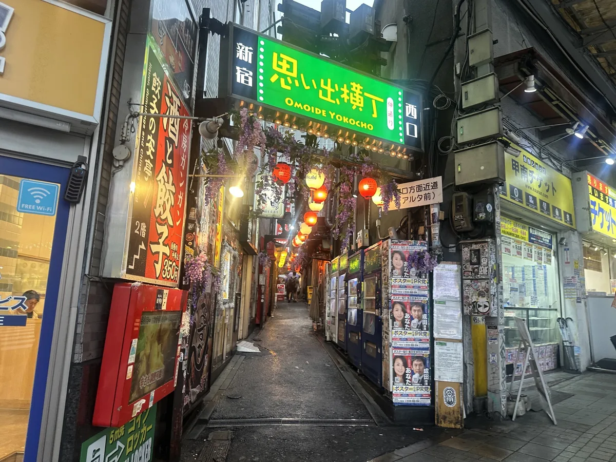 The narrow Omoide Yokocho alley in Shinjuku with its green neon sign and small izakaya fronts, in 2024