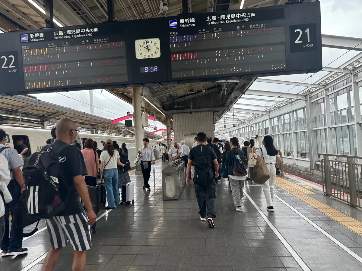 Passengers on the Sanyo Shinkansen platforms at Okayama Station under departure boards for trains to Hiroshima, Hakata and.