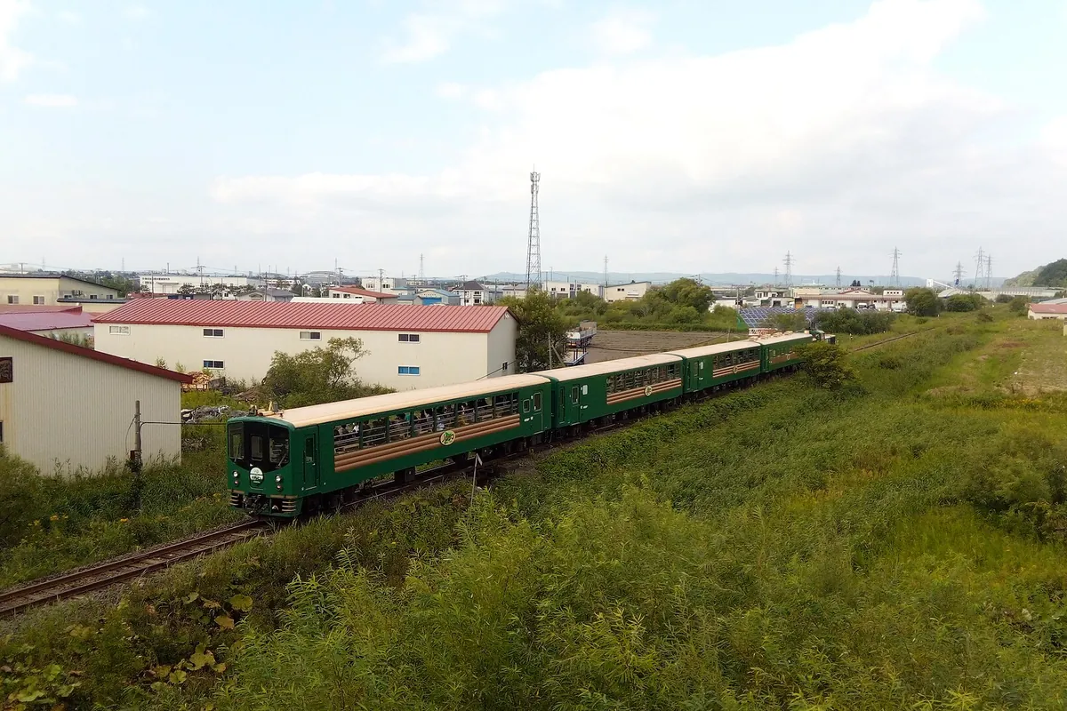 綠色的慢車號觀光列車行經草地、民宅與輸電鐵塔的空拍畫面