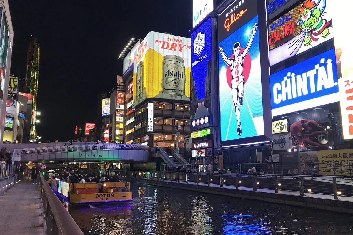 The Dotonbori canal in Osaka at night with the Glico running man sign, other neon signs, and a boat on the water