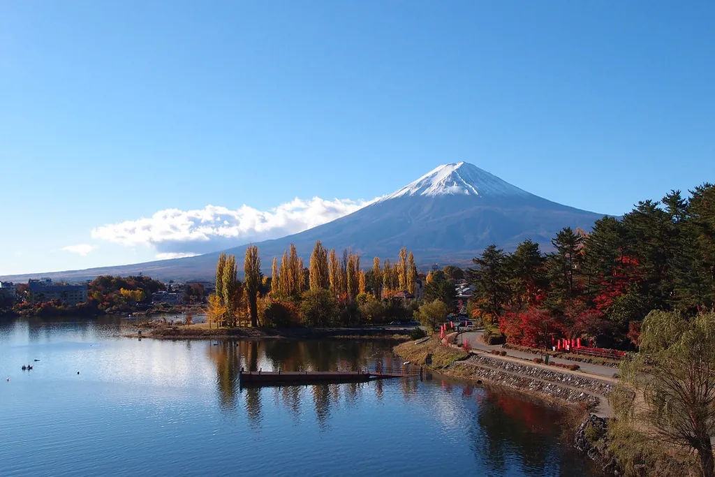Mount Fuji seen across Lake Kawaguchi with autumn-colored trees lining the shoreline in the foreground