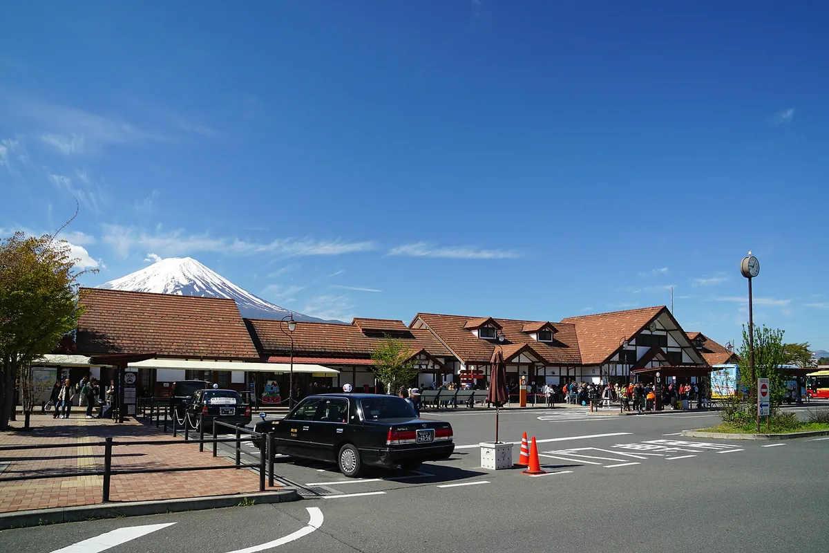 Kawaguchiko Station building with people and a taxi outside, Mount Fuji visible above the rooftop