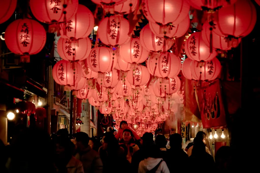 Rows of red paper lanterns lit at night over a street in Nagasaki, with a crowd of people walking below