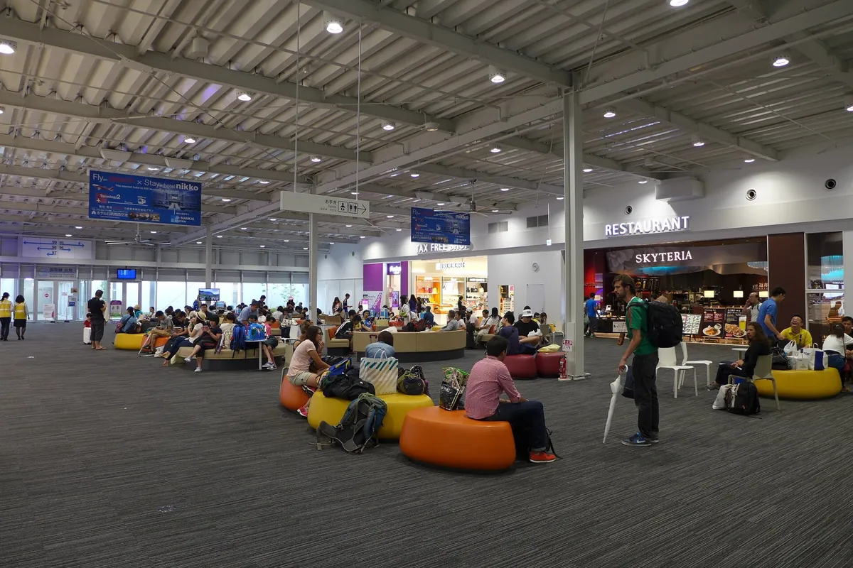 A spacious departure hall with orange seating and shop signage at Kansai International Airport Terminal 2