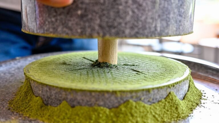 A stone mill grinding tea leaves into matcha powder piled around its base