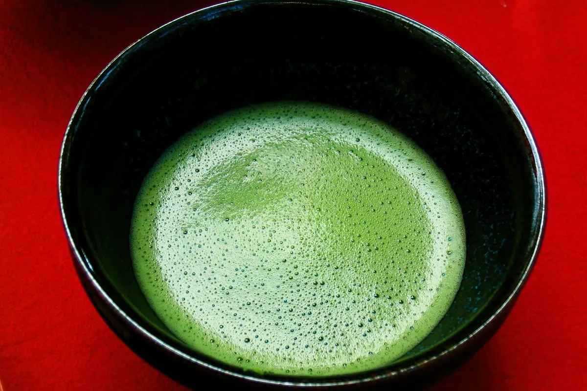 A black bowl of frothy whisked matcha viewed from above on a red surface