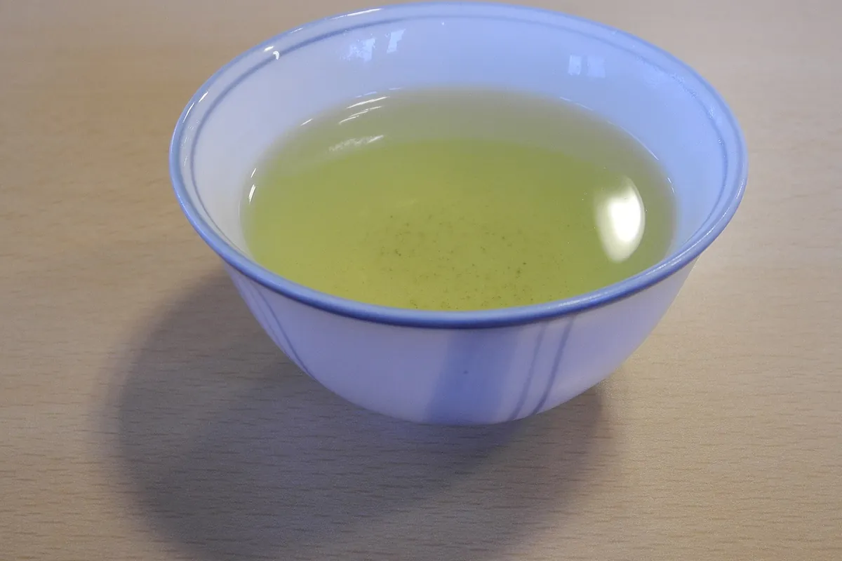 A white tea cup with a blue rim filled with pale green tea, on a wooden table.