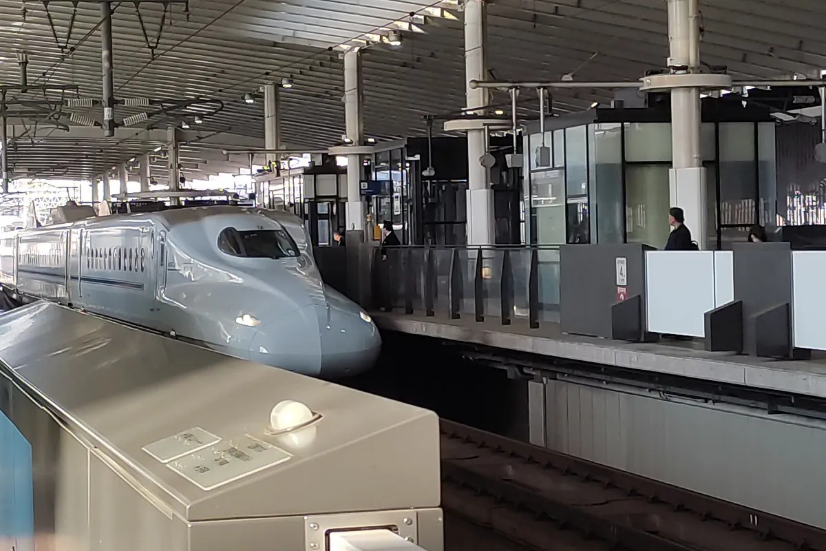 An N700 series Shinkansen train arriving at a station platform with passengers waiting nearby