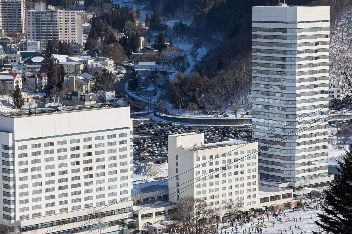 高層ホテルや駐車場、下に見えるスキーヤーを含む、雪に覆われたリゾートタウンの空撮