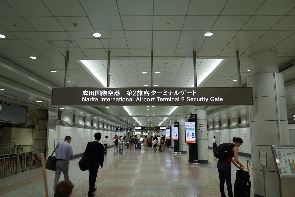 Travelers walking past the Narita International Airport Terminal 2 Security Gate sign