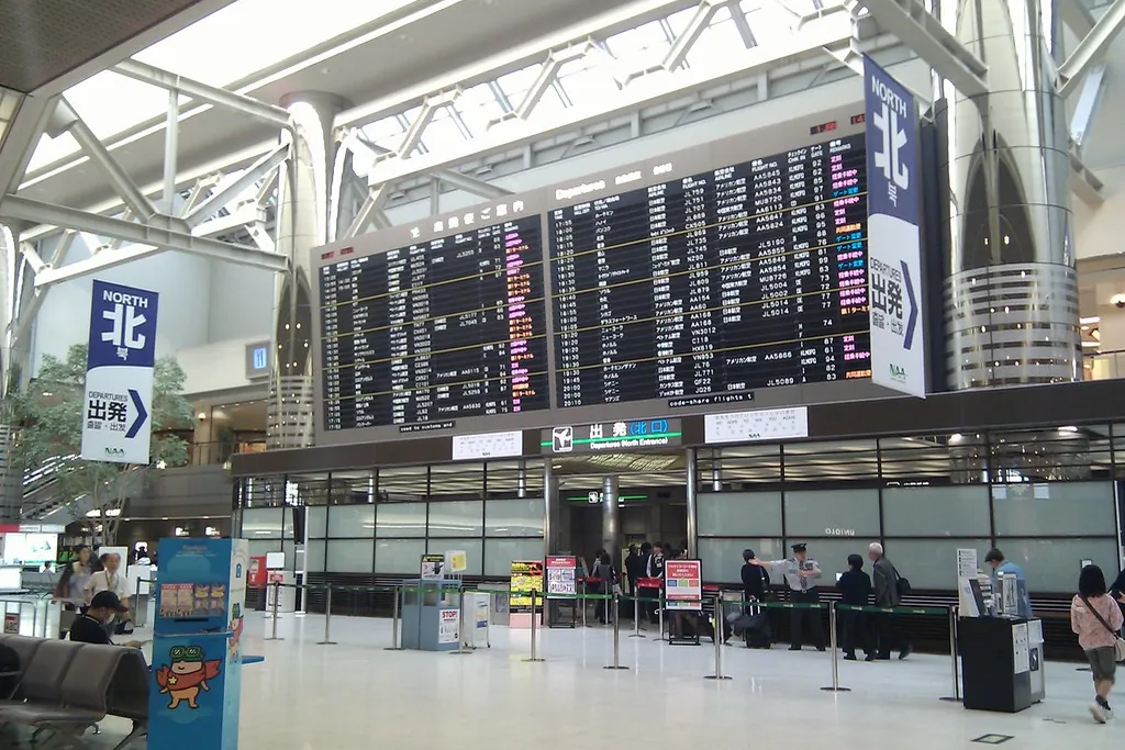 Large departure board above the North Entrance of Narita Airport, with passengers queuing behind barrier posts
