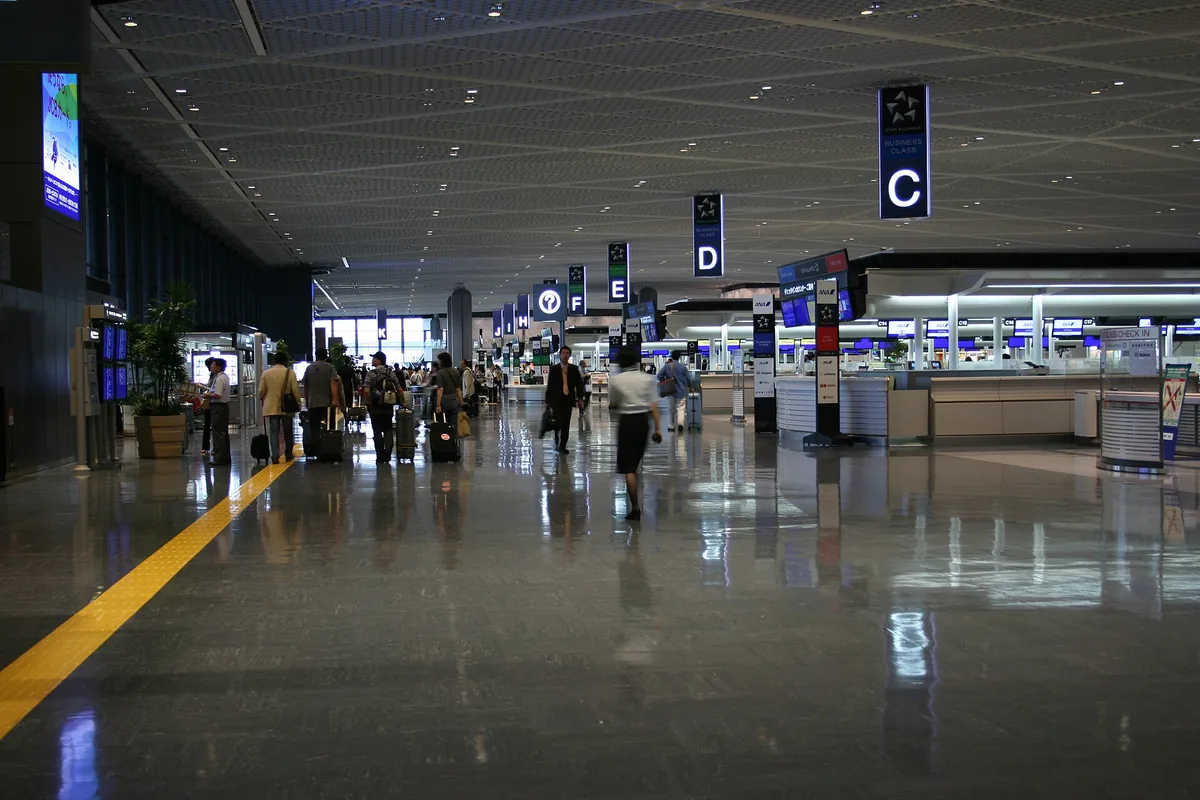 Travelers with rolling suitcases in a large Narita Airport departure hall, with check-in counters on the right
