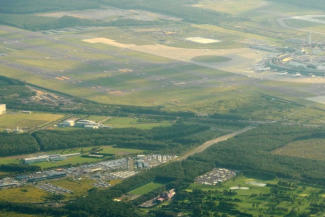 Aerial view of New Chitose Airport's terminal buildings and runway surrounded by forest in Hokkaido