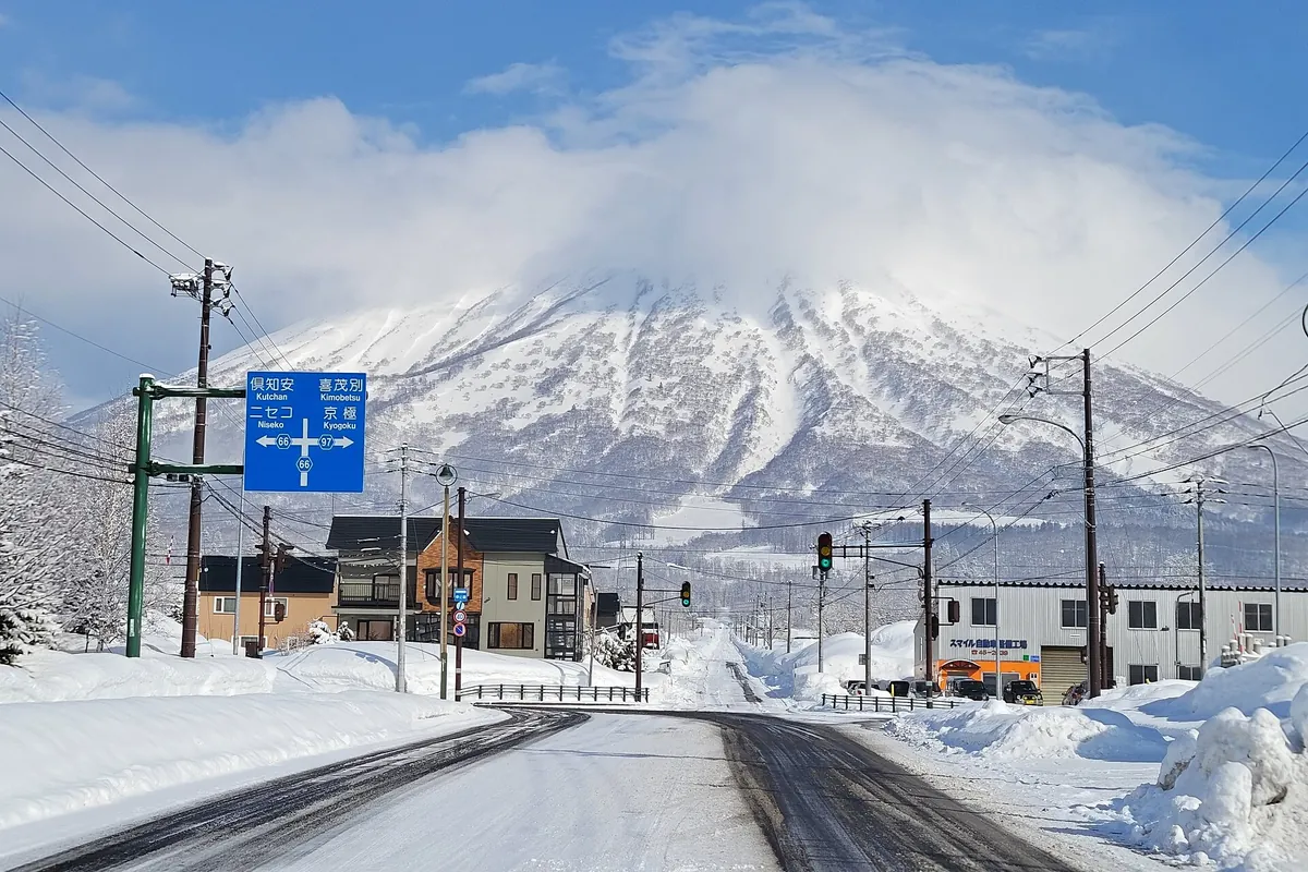 Snow-covered road leading toward snow-capped Mt. Yotei, lined with houses in a Hokkaido town