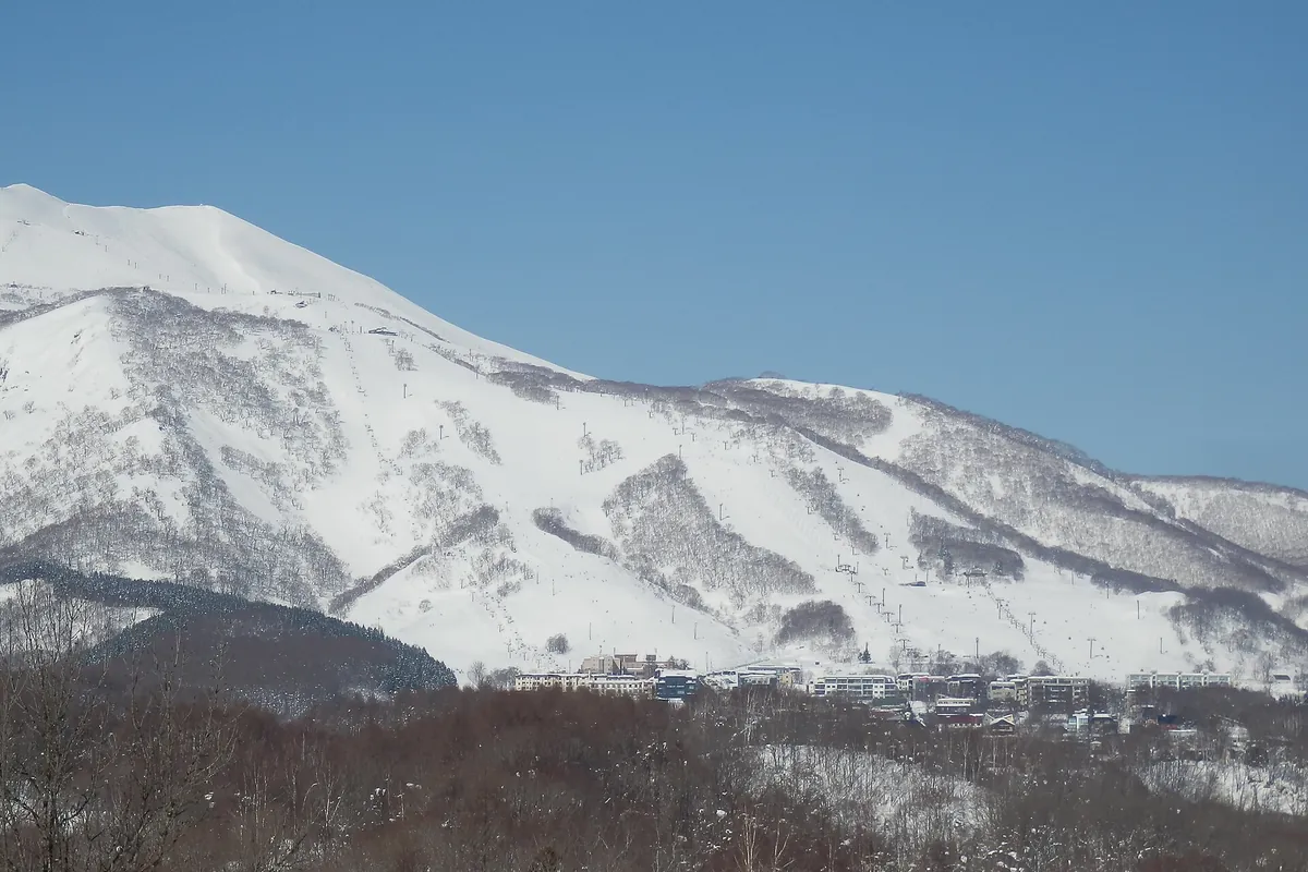 Snow-covered ski slopes on a mountainside above Niseko Hirafu, with resort buildings at the base