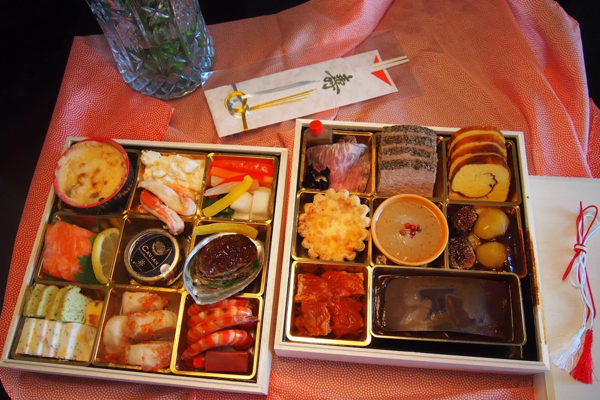 いくつもの仕切りがある2つの四角い箱に盛られた色鮮やかなおせちと箸