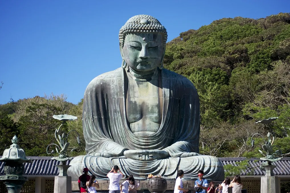 The bronze Great Buddha of Kamakura seated outdoors at Kotoku-in temple, with visitors and wooded hills behind