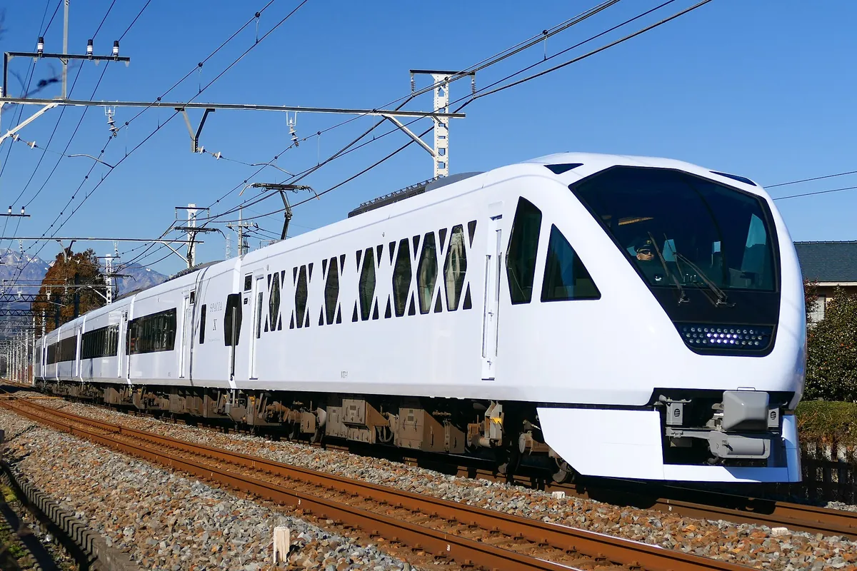 A white Tobu SPACIA X limited express train running along the tracks, with overhead power lines above