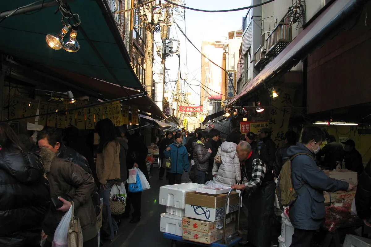 Shoppers walking through a narrow covered lane lined with small food stalls at Tsukiji Outer Market in Tokyo