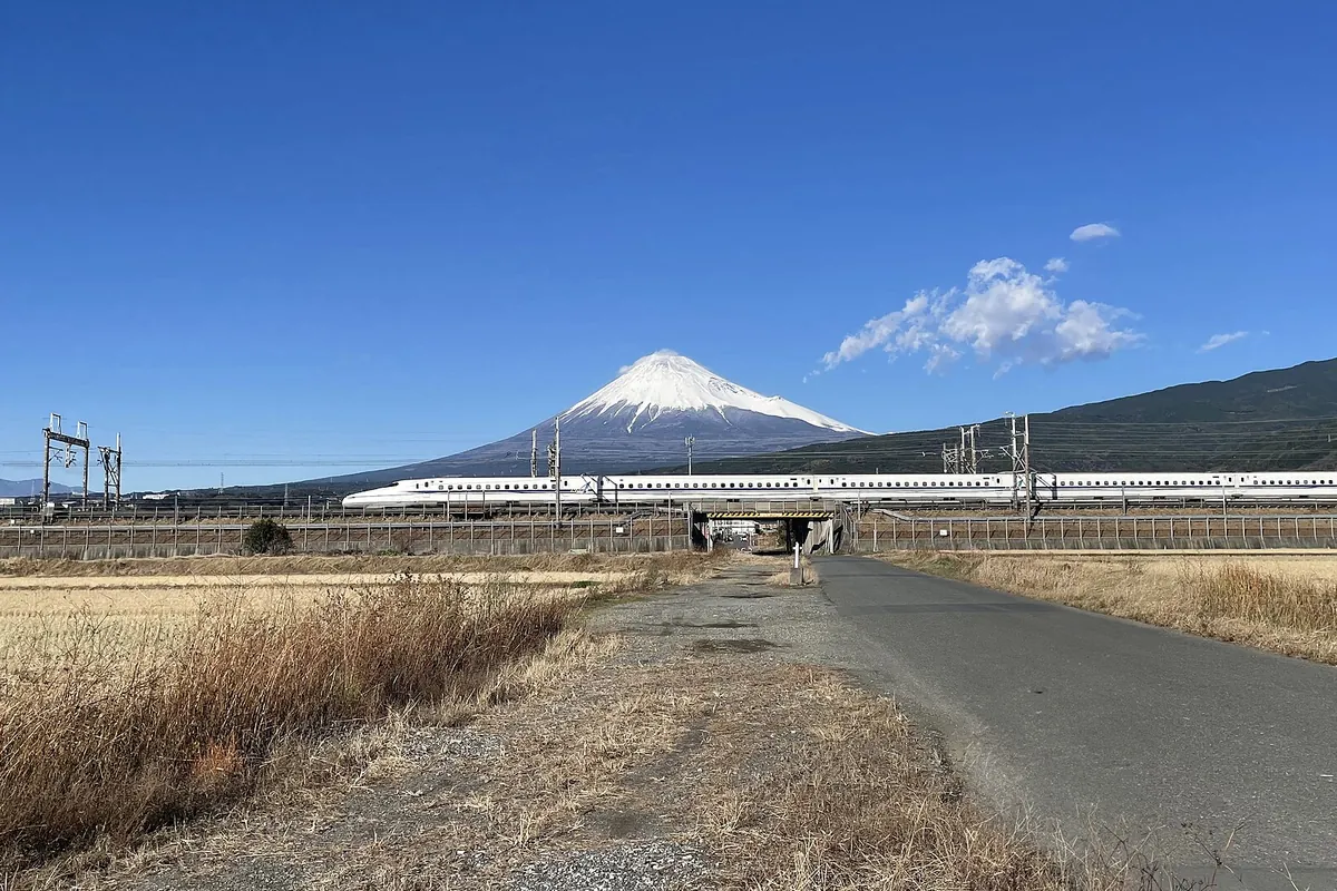 A Shinkansen train crossing an elevated track with snow-capped Mount Fuji in the background