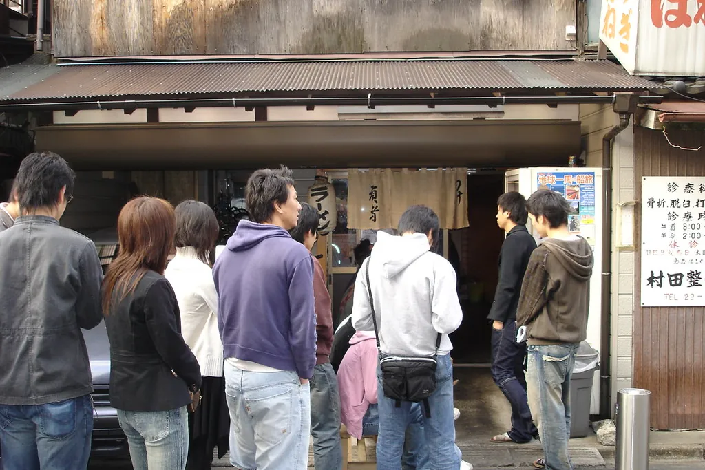 People queuing outside a shop entrance on a street in Japan, seen from behind and the side.