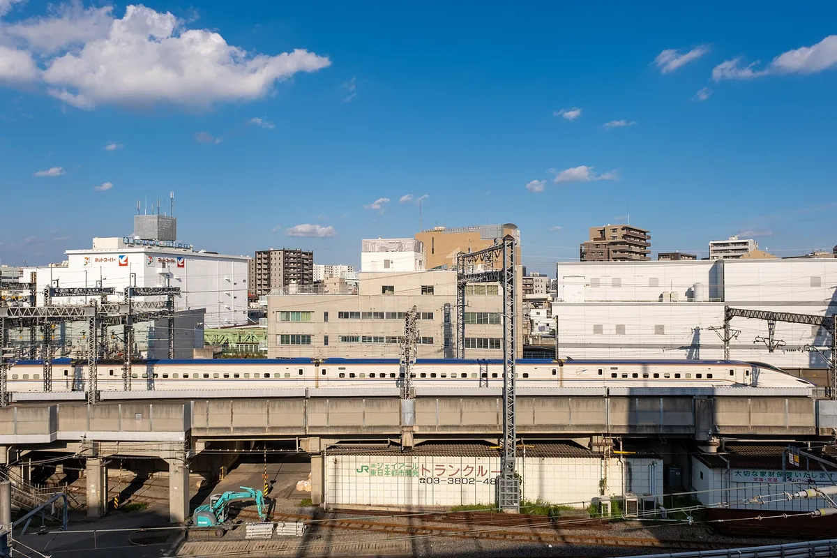 A white Shinkansen train on elevated tracks passing through a Tokyo neighborhood with office and apartment buildings