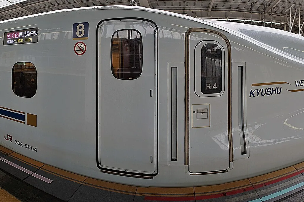 Close-up of a white Shinkansen train car with KYUSHU lettering, a number 8 platform sign, and a no-smoking sign on the door