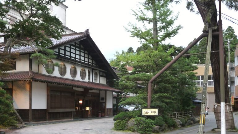 石畳の小道と木々に囲まれた、伝統的な木造旅館の入り口