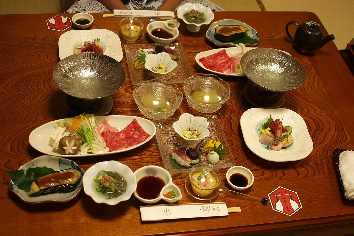 旅館の低いテーブルに並べられた、季節の小さな料理がたくさん並ぶ懐石料理の夕食