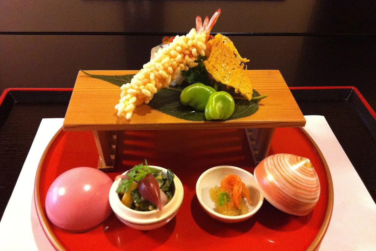 A kaiseki course with tempura on a wooden stand, served alongside small dishes on a red tray